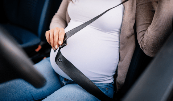 Closeup of pregnant woman sitting in car and fasten seat belt