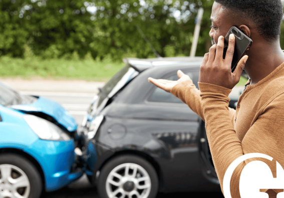 Man on the phone in the foreground with a car collision in the background